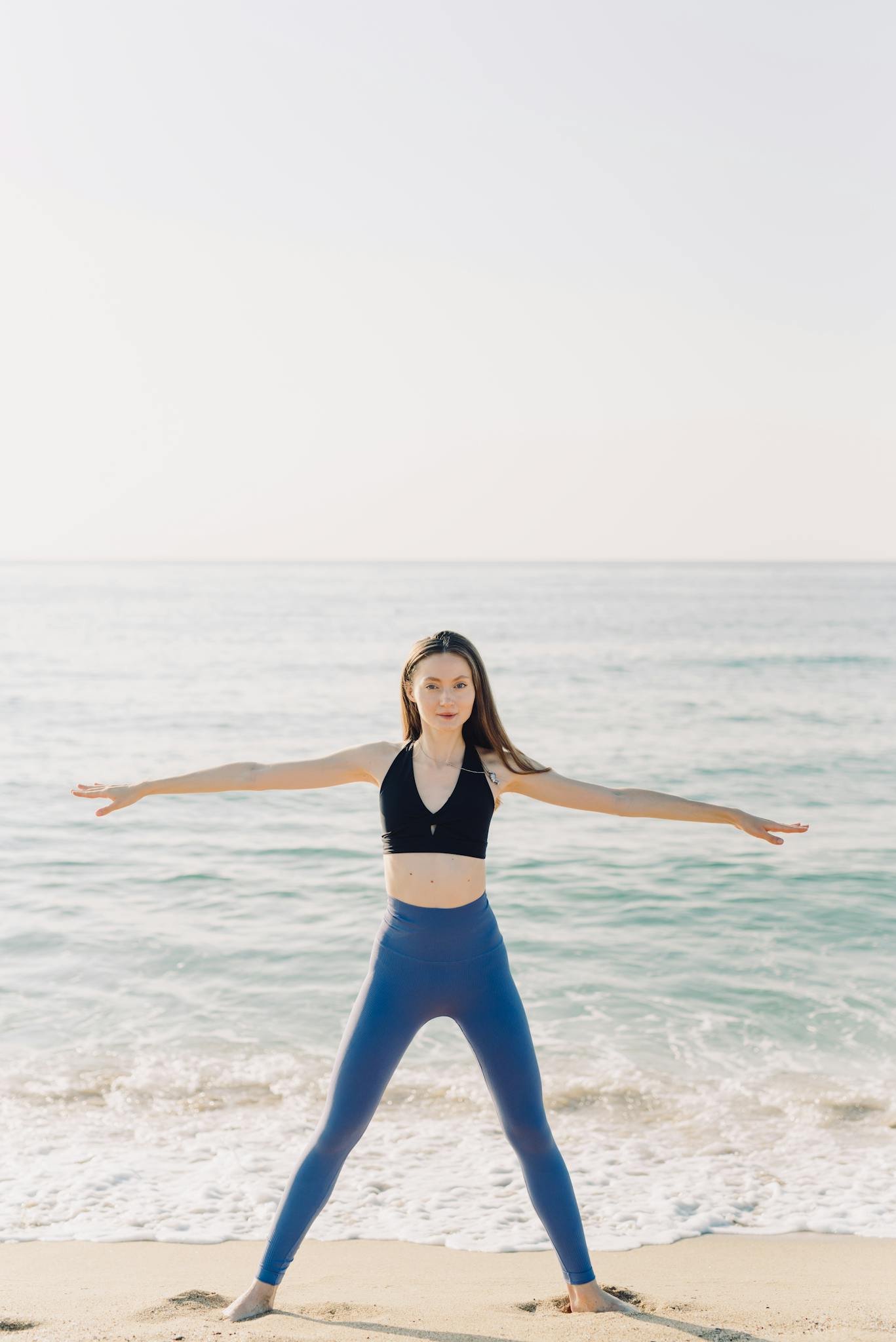 Woman in yoga pose enjoying ocean view on a sunny beach, promoting wellness and healthy lifestyle.